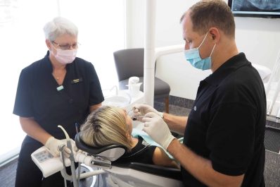 Two dental professionals, wearing masks and gloves, attend to a patient in a dental chair. Dentists Tauranga